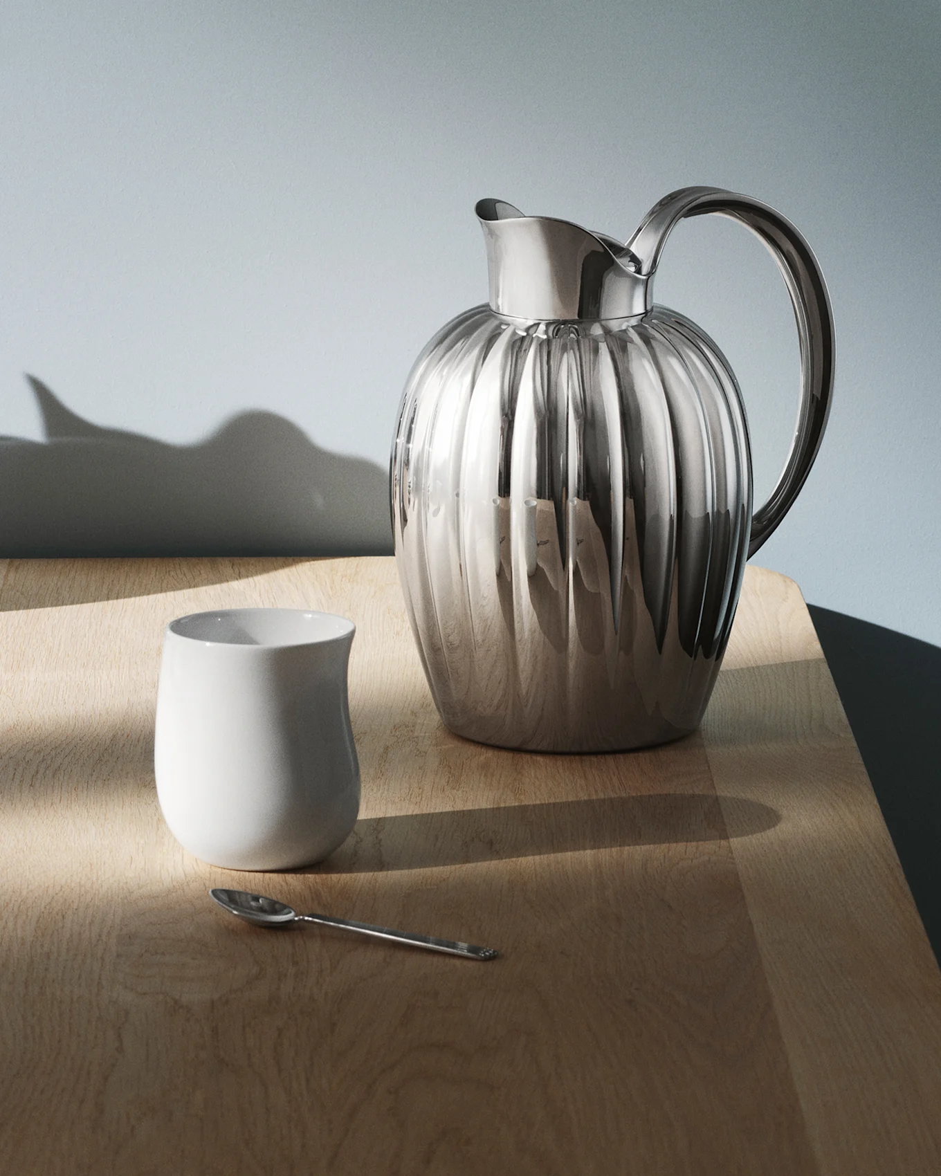 Błyszczący, żebrowany srebrny dzbanek z uchwytem na ciemnym, odblaskowym stole, z wzorami światła na powierzchni.