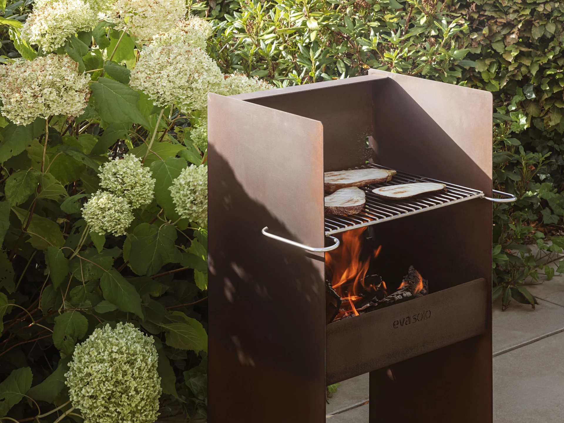 Rustykalny, metalowy grill ogrodowy z płomieniami i plasterkami bakłażana piekącymi się na ruszcie.