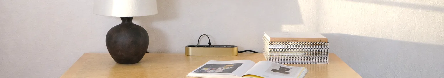 Złota listwa zasilająca z trzema czarnymi gniazdkami i przyciskiem zasilania na jasnej powierzchni.