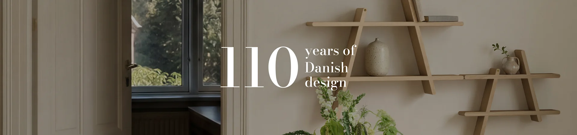 Tekst '110 years of Danish design' na zdjęciu wnętrza pokoju z geometryczną drewnianą półką, wazonem i kwiatami.