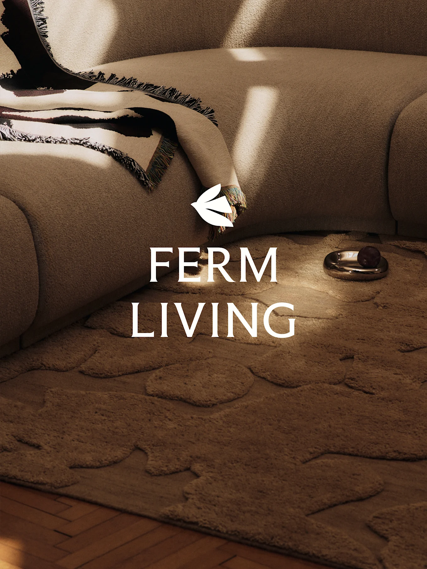 Przytulna scena z jasnobrązową teksturowaną sofą, wzorzystym kocem, brązowym dywanem o organicznych kształtach i ozdobnym naczyniem.