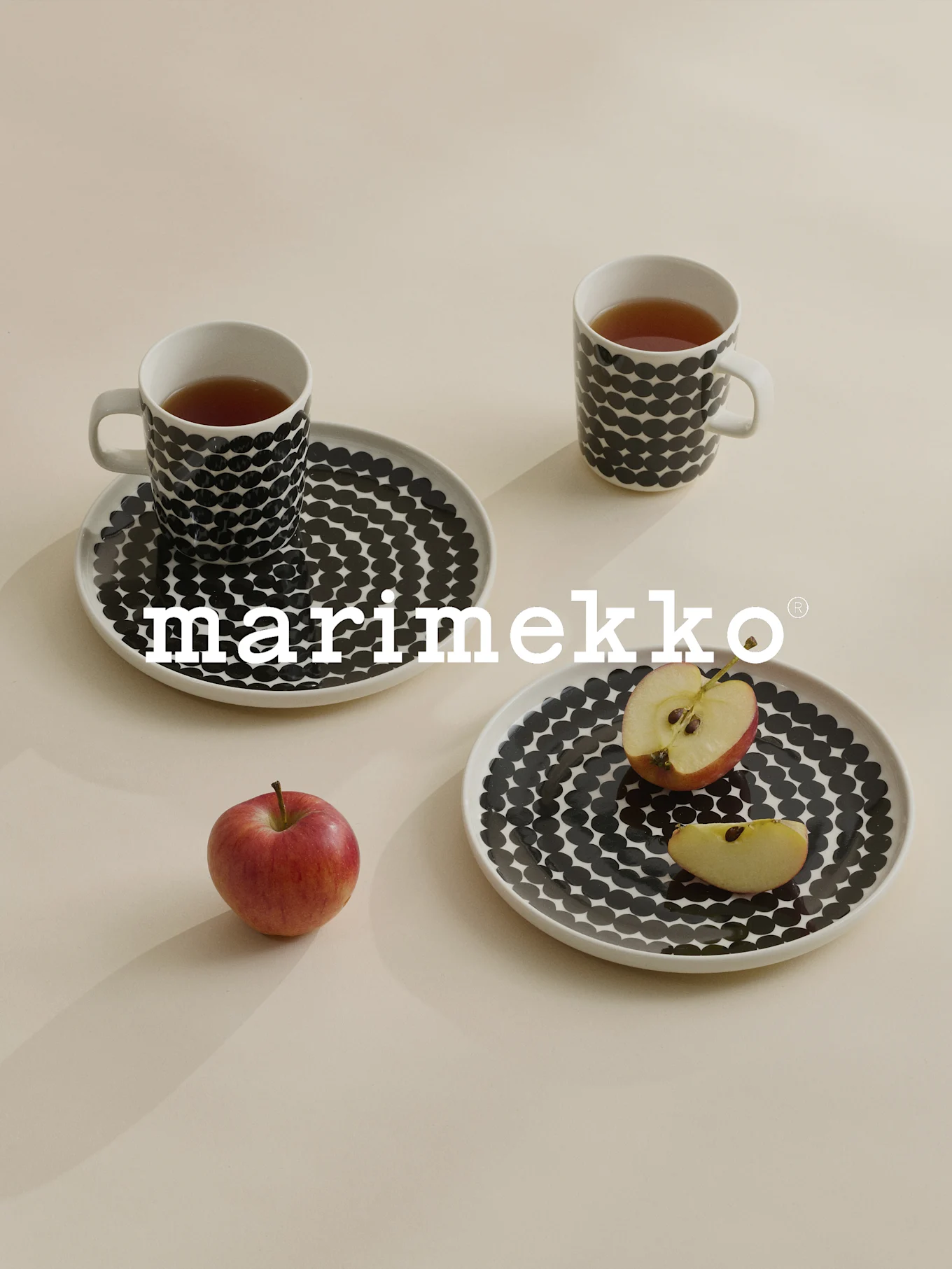 Dwa kubki i talerze w czarne kropki, herbata, czerwone jabłko, logo Marimekko.