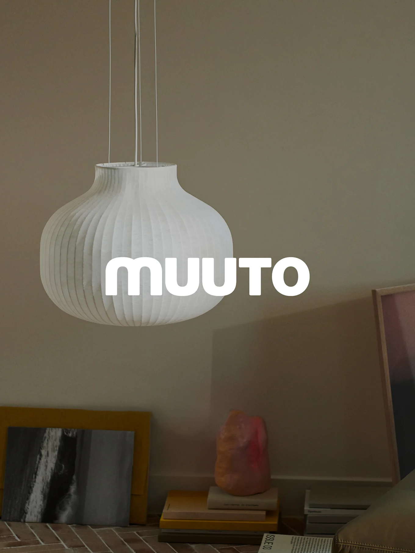 Biała prążkowana lampa wisząca w kształcie tykwy z logo 'MUUUTO', w beżowym pokoju.