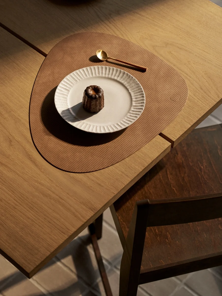 Widok z góry: canelé na białym talerzu, złota łyżka na teksturowanej brązowej podkładce na drewnianym stole.