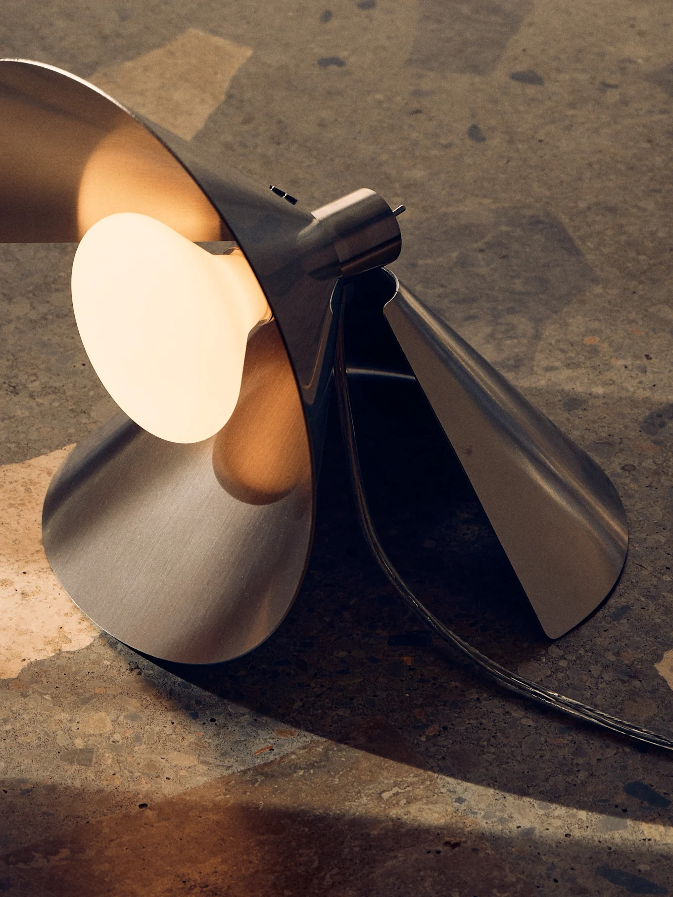 Nowoczesna lampa stołowa z szczotkowanego metalu, rzeźbiarski, złożony design, ciepła żarówka na teksturowanej powierzchni.
