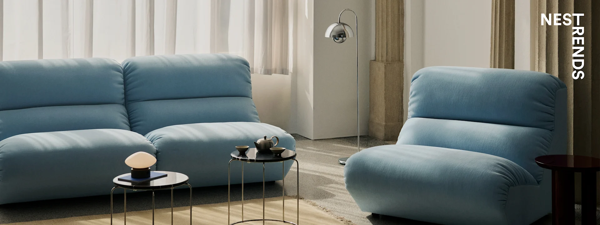 Nowoczesny salon z dwiema jasnoniebieskimi sofami, czarnymi marmurowymi stolikami i eleganckimi lampami.