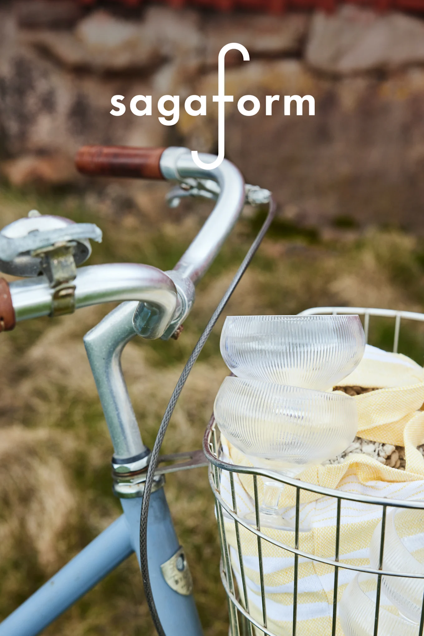 Dwie przezroczyste, żebrowane szklane miski i żółty ręcznik w paski w koszyku rowerowym. Logo „sagaform”.