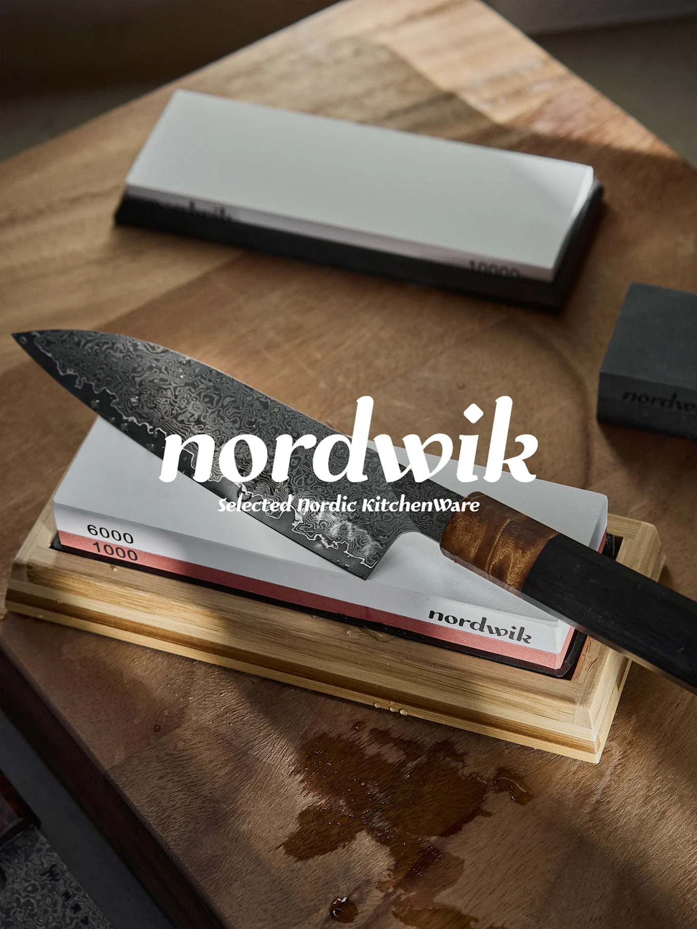 Nóż szefa kuchni damasceński na kamieniu do ostrzenia o ziarnistości 1000 i 6000, na mokrej drewnianej powierzchni.