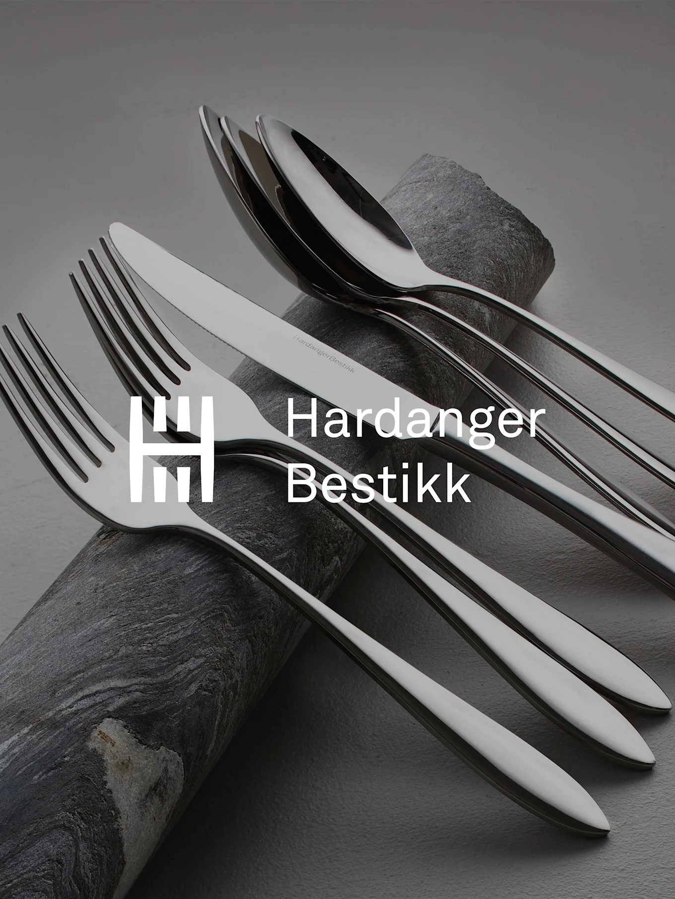 Błyszczący zestaw sztućców ze stali nierdzewnej, zawierający widelce, noże i łyżki, artystycznie ułożony na ciemnym, teksturowanym kamieniu.