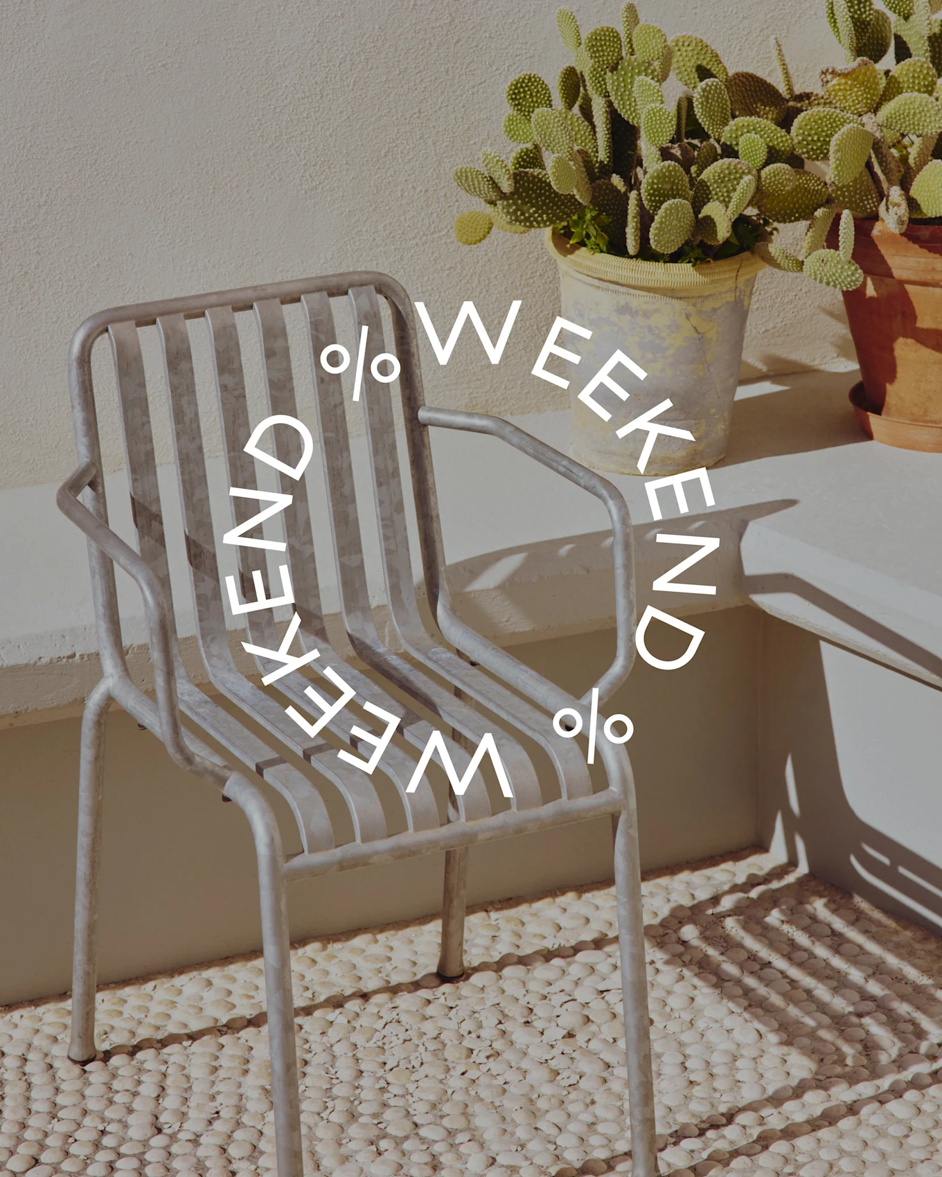 Szare metalowe krzesło lamelowe obok doniczkowego kaktusa, z okrągłym tekstem 'WEEKEND % WEEKEND %'.