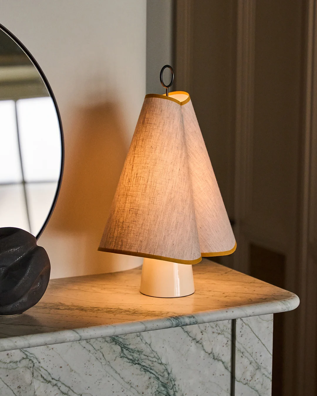 Unikalna lampa stołowa z podwójnym stożkowym abażurem z tkaniny obszytym na żółto, rzucająca ciepły blask na zielony marmurowy blat.