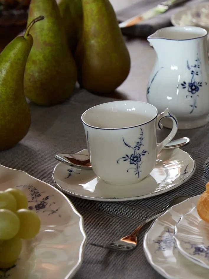 Biała porcelanowa filiżanka, spodek i dzbanek z niebieskim wzorem kwiatowym na stole z gruszkami i winogronami.