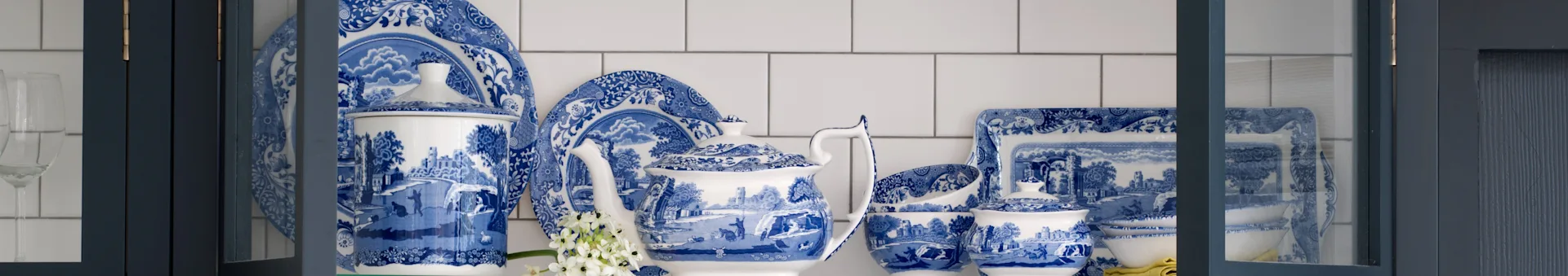 Zestaw porcelanowej zastawy stołowej w niebiesko-białe wzory z czajnikiem, talerzami i miskami w granatowej szafce.