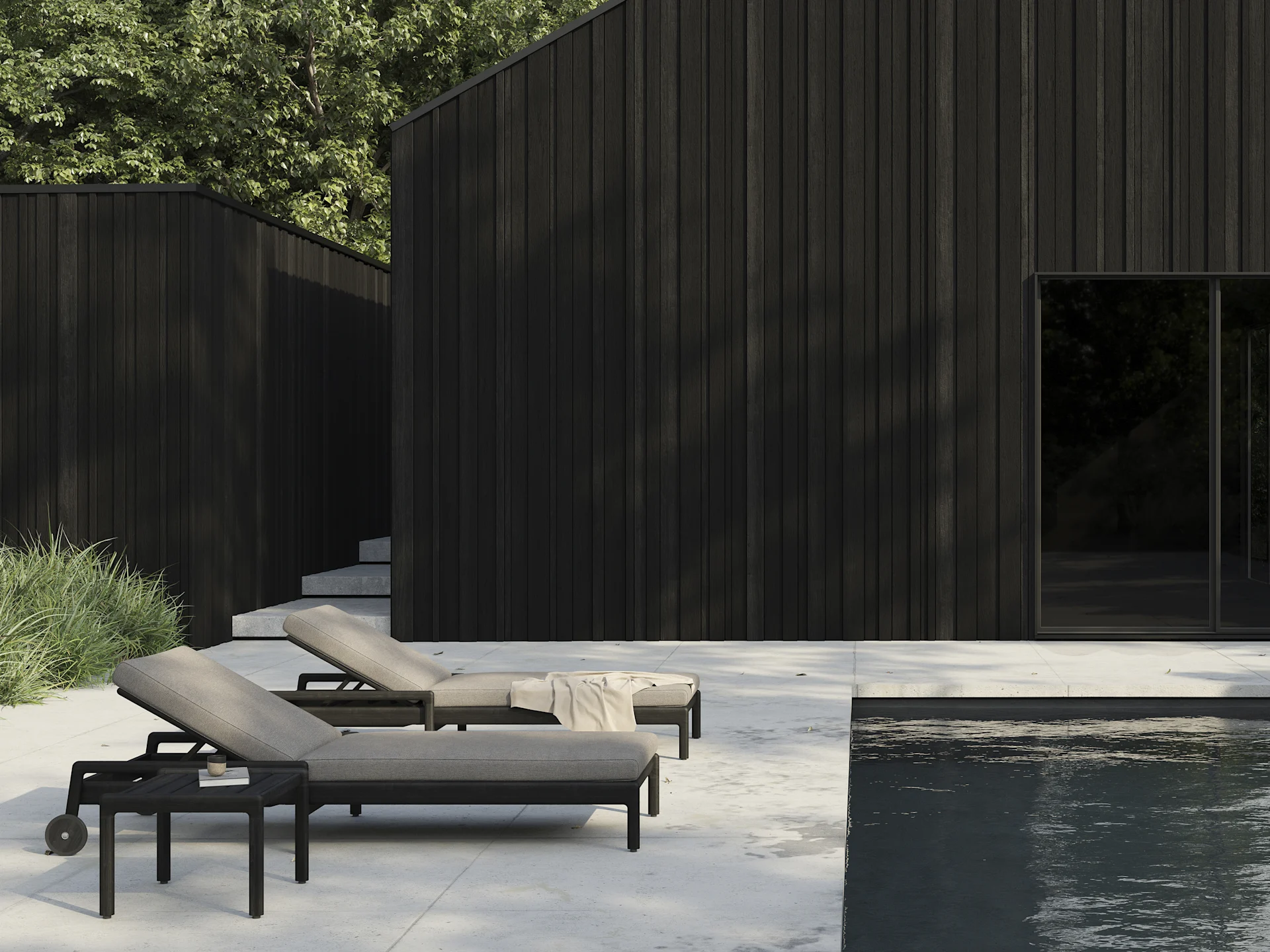 Dwa ciemne leżaki z jasnymi poduszkami na patio obok basenu, z nowoczesnymi, ciemnymi budynkami drewnianymi w tle.