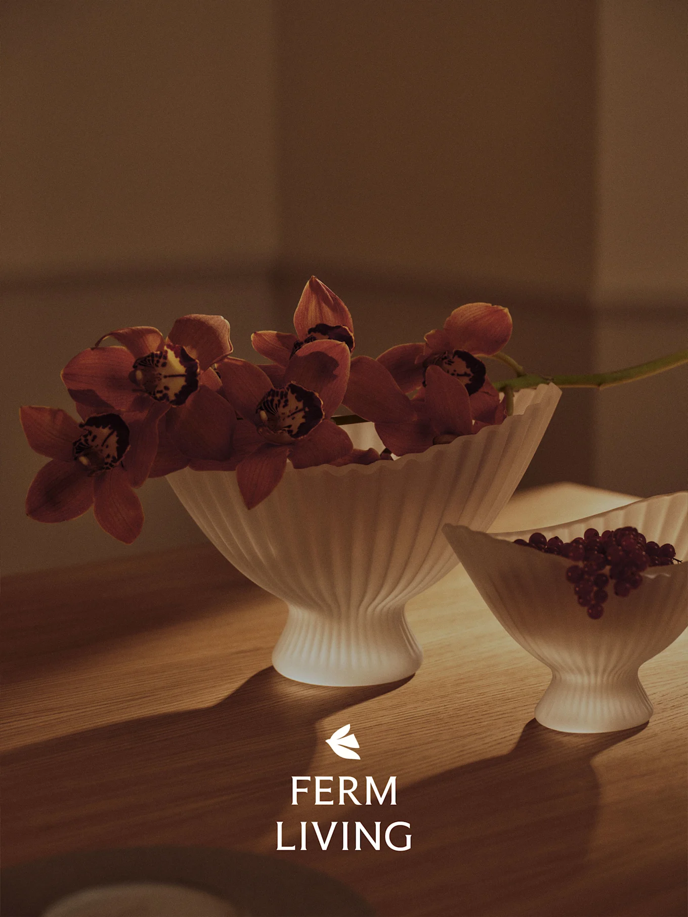 Dwie ryflowane białe miski na drewnianym stole, jedna z czerwonymi orchideami, druga z czerwonymi jagodami, w ciepłym świetle.