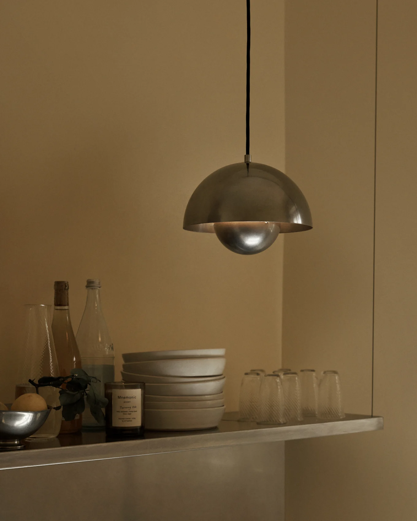 Lampa wisząca z kopułą ze szczotkowanego metalu wisi nad półką z miskami, butelkami i szklankami.