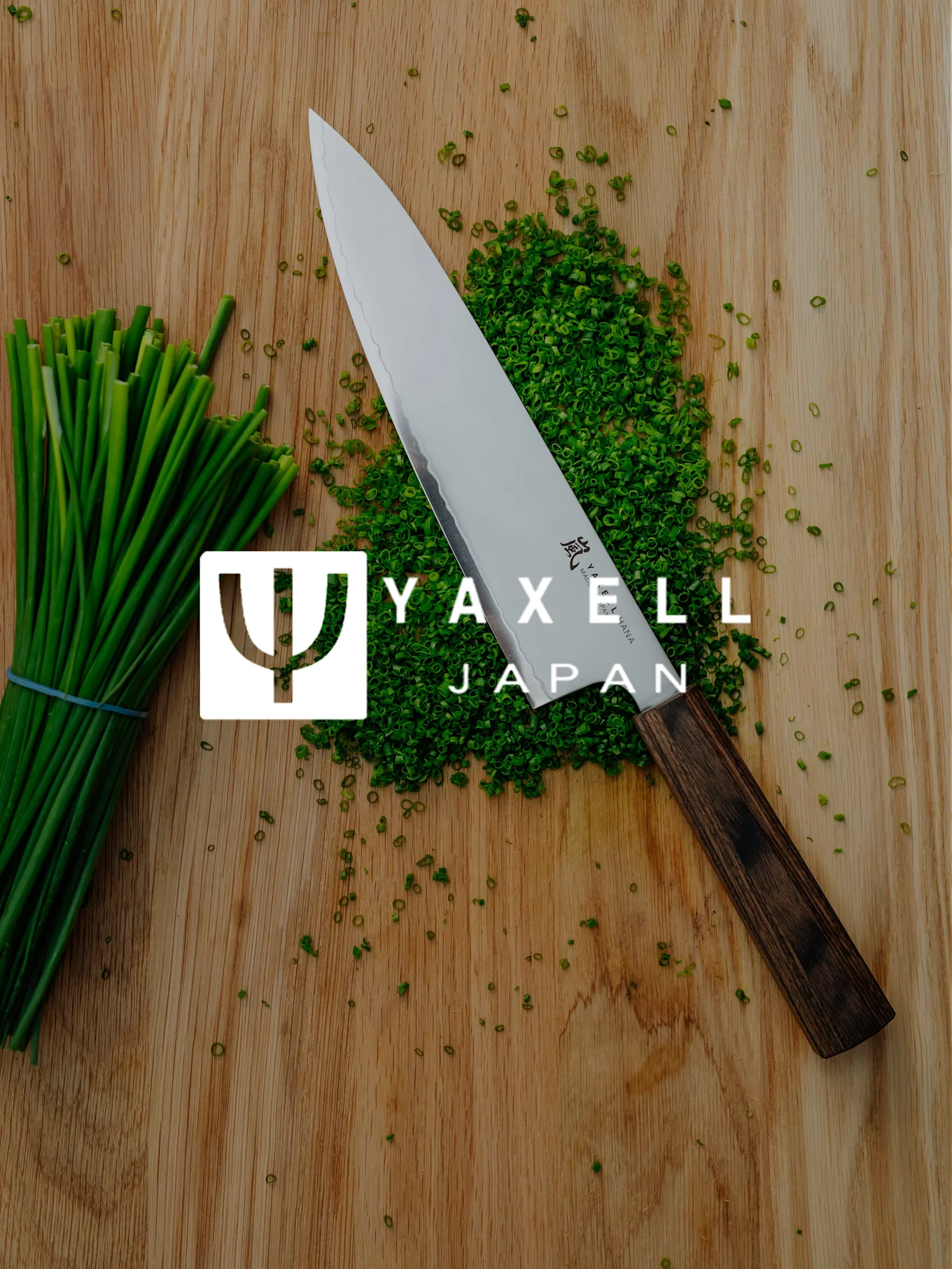 Nóż szefa kuchni Yaxell, posiekany szczypiorek i pęczek szczypiorku na drewnianej desce z logo Yaxell Japan.