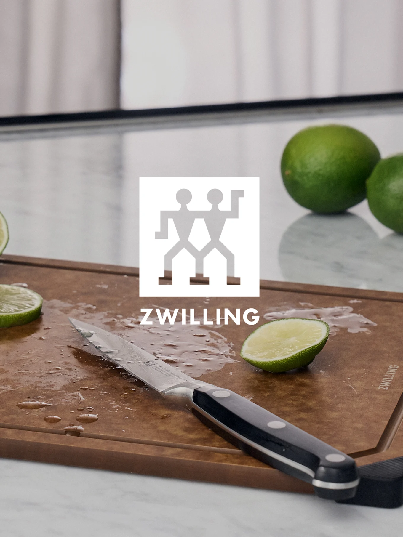 Logo ZWILLING nad deską do krojenia z nożem, pokrojoną limonką i całymi limonkami.