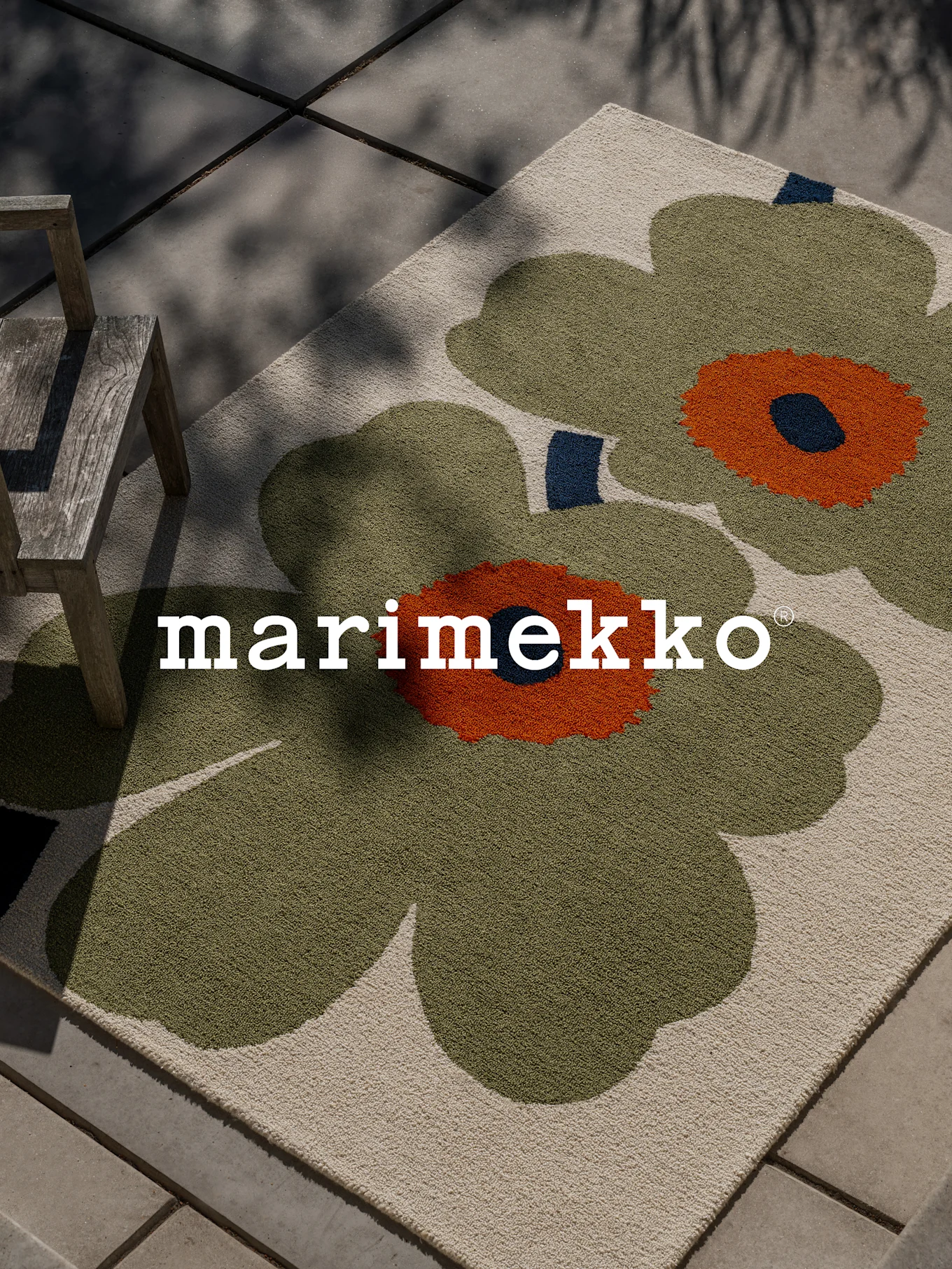 Dywan Marimekko z dużym zielono-pomarańczowym wzorem kwiatowym na patio z drewnianym krzesłem.